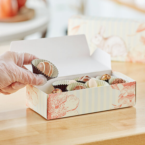 A hand holding a 1 lb. Vintage Rabbit Print Candy Box filled with chocolate candy.