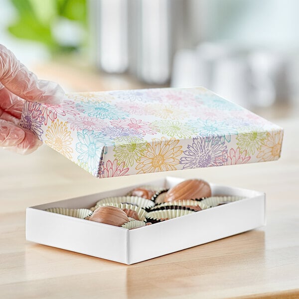 A gloved hand holding a 1/2 lb. spring print candy box with colorful flowers on it.