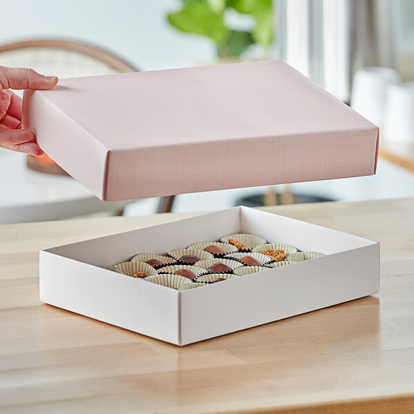 A hand holding a pink linen candy box with chocolates inside.