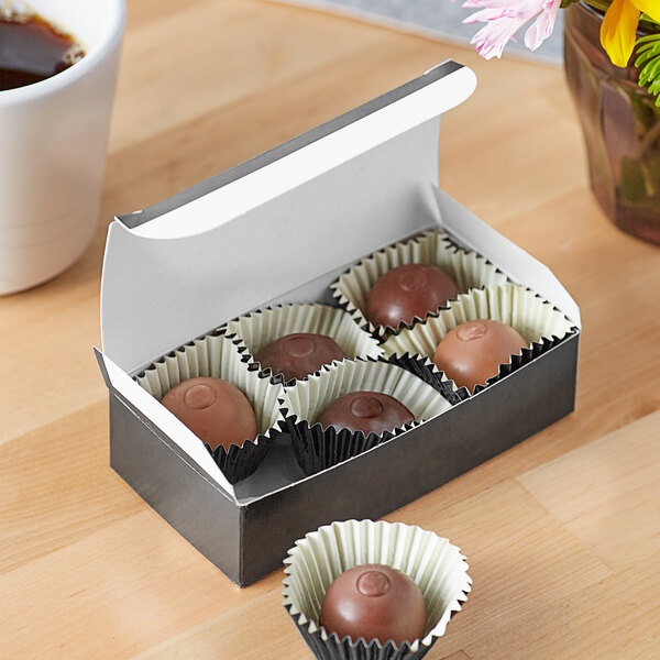 A black candy box filled with chocolate-covered chocolates on a table.