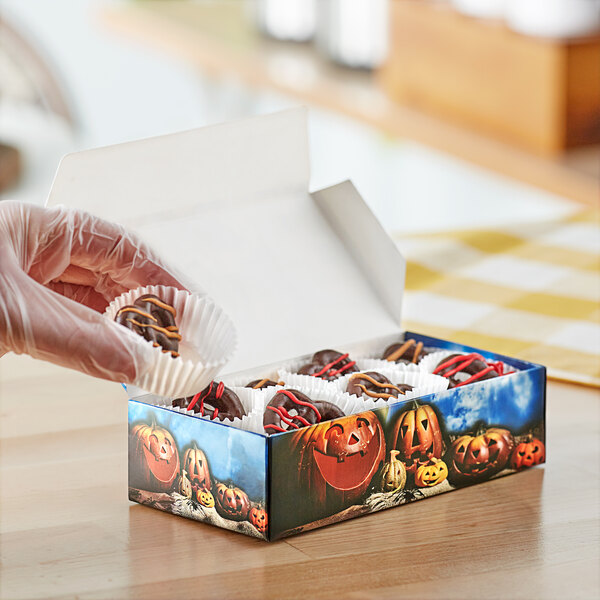 A hand holding a Jack-O'-Lantern print candy box filled with chocolates.