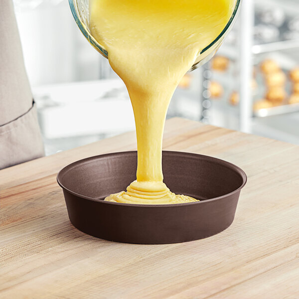 A bowl of yellow cake batter being poured into a Gobel round cake pan.