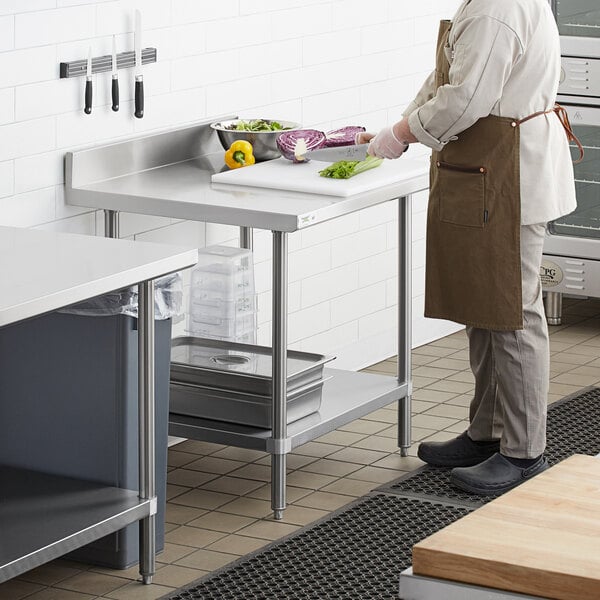A man in a brown apron using a Regency stainless steel work table with undershelf to cut vegetables.