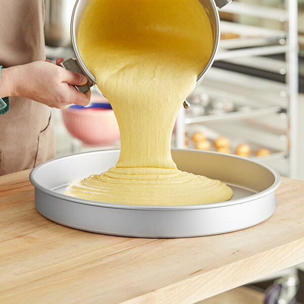 A person pouring cake batter into a Fat Daddio's round cake pan.