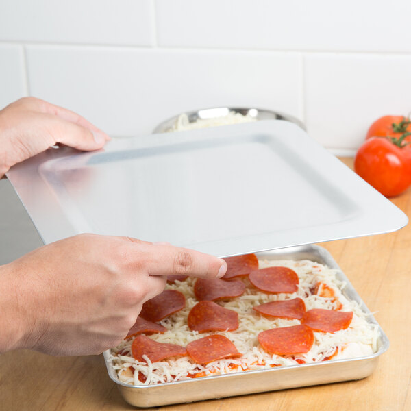 A person holding a tray of pizza with a square deep dish pizza pan lid.