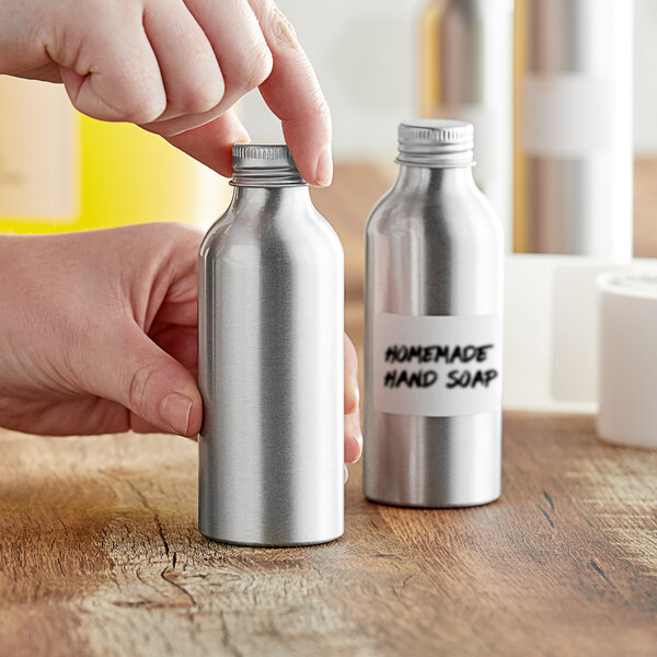 A hand putting a label on a silver aluminum squat bottle.