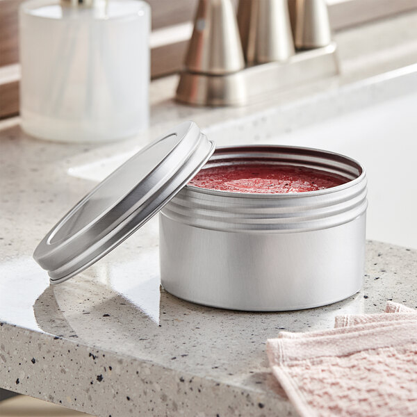 A silver container with a lid open on a counter containing red liquid.