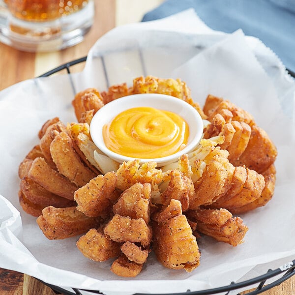 A basket of Golden Dipt Zesty fried onion rings with a dipping sauce on a table.