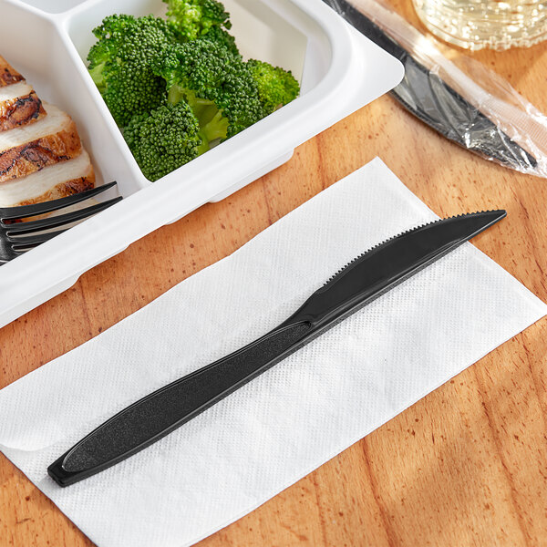 A white tray with a black handle and a Solo Impress black plastic knife and fork on a white napkin.
