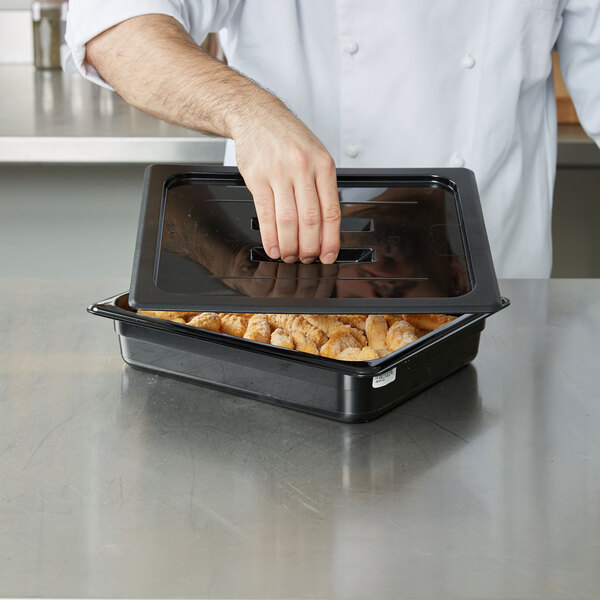 A person using a black Cambro polycarbonate lid to cover a container of food.