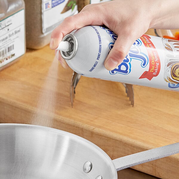 A person spraying Baker's Joy release spray onto a silver pan.
