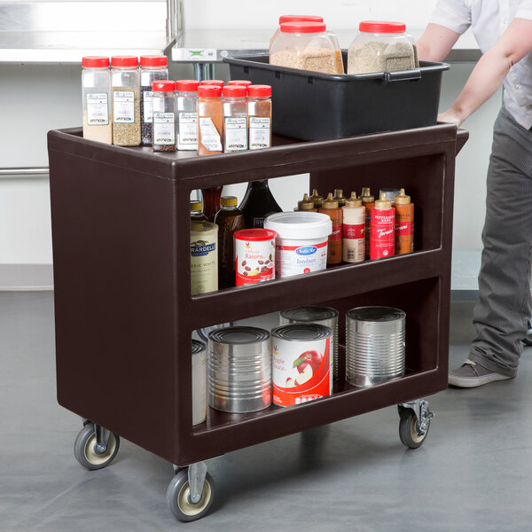 A dark brown Cambro utility cart with food containers and cans on it.