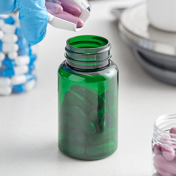 A person in blue gloves holding a 120cc green PET packer bottle filled with pills.