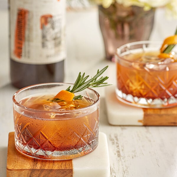 Two glasses of DaVinci Gourmet Old Fashioned drinks with rosemary and orange slices on a white and wood surface.