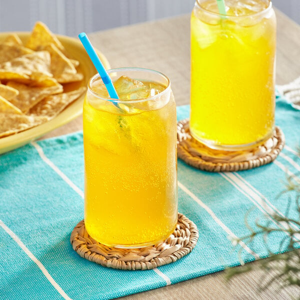 A pair of glasses filled with Jarritos Mango soda and straws on a table with chips.