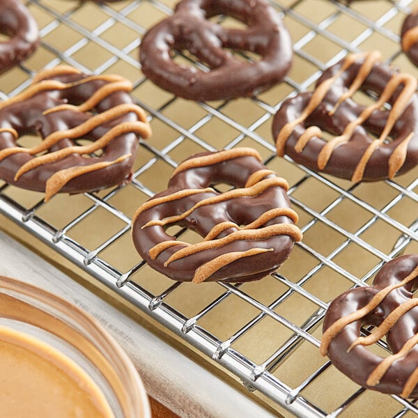 Chocolate covered pretzels on a metal cooling rack with Alpine Peanut Coating Wafers.