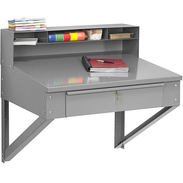 A grey Tennsco wall-mounted shipping/receiving desk with a drawer, shelf, and book.