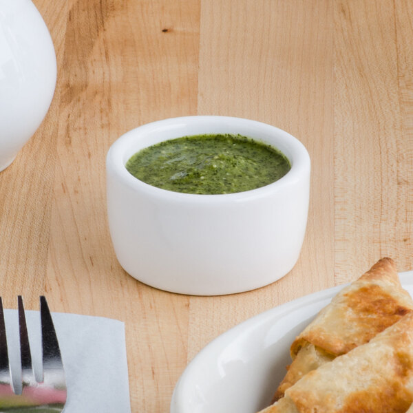 A plate of food with a Tuxton white ramekin of green sauce on a table.