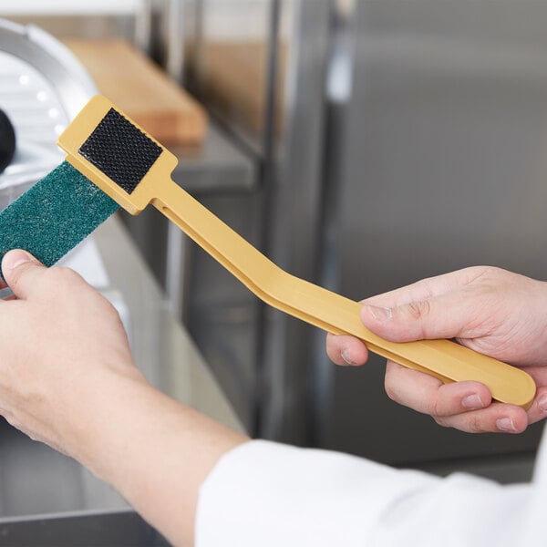 A person using a Carlisle Sparta Easy Slicer Cleaning Tool to clean a meat slicer.