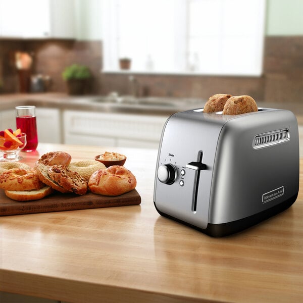 A KitchenAid Contour Silver toaster with bread on top of it next to a plate of bagels.