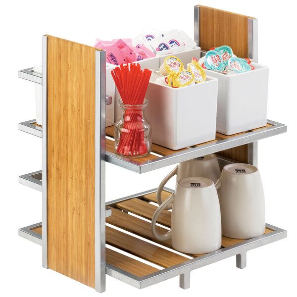 A Cal-Mil wooden two-tier merchandiser on a counter with white mugs on the top shelf and glass jars on the bottom shelf.