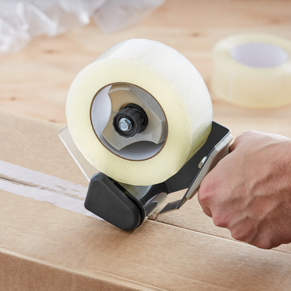 A hand using a Lavex Pro tape dispenser to seal a box with clear tape.