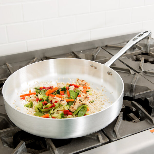 A Vollrath Wear-Ever saute pan with vegetables and rice on a stove.