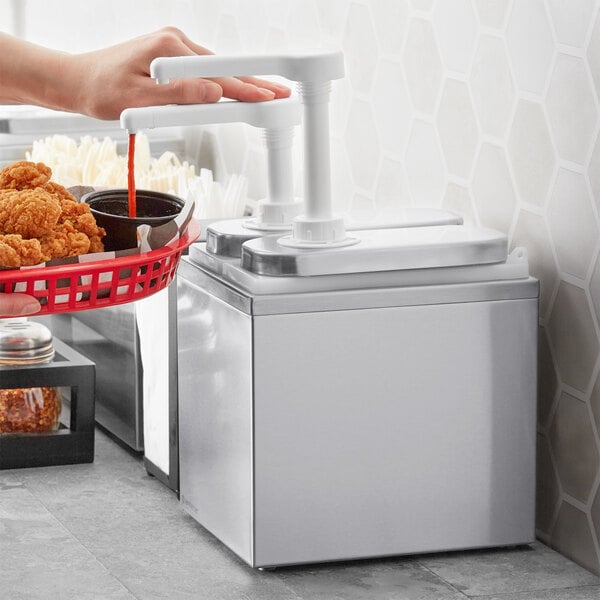 A person using a ServSense stainless steel condiment dispenser to pour sauce into a basket of fried chicken.
