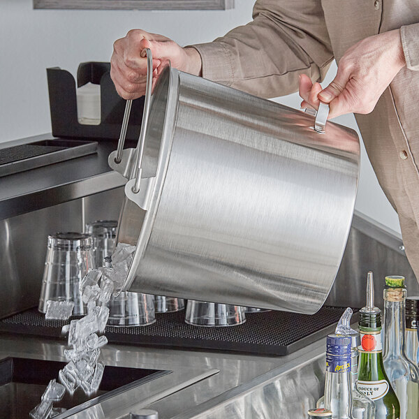 A man pouring ice into a Vollrath stainless steel dairy bucket on a counter.