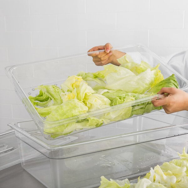 A person using a Cambro clear polycarbonate colander pan to hold lettuce.