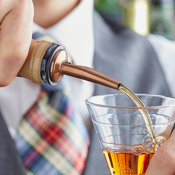 A person using an Acopa copper liquor pourer to pour liquid into a glass.