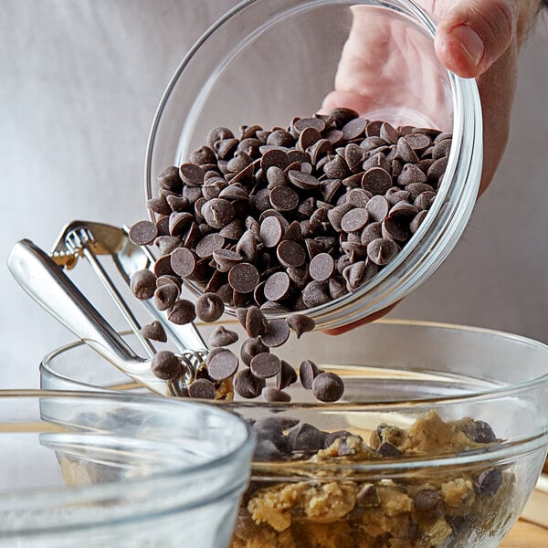 A hand pouring Nestle Semi-Sweet 1M chocolate chips into a glass bowl.