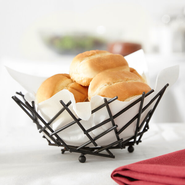 An American Metalcraft round black wire basket filled with rolls of bread on a counter.