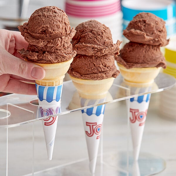 A hand holding a JOY cake cone with chocolate ice cream in it.