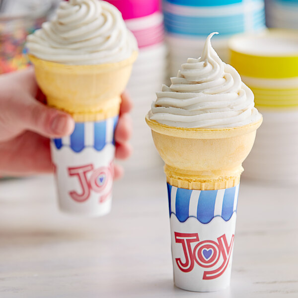 A hand holding two JOY flat bottom cake cones filled with ice cream.