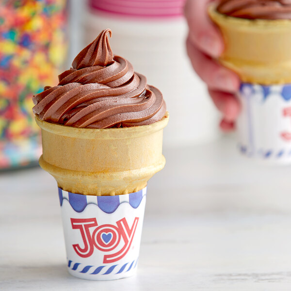 A chocolate ice cream cone in a brown flat bottom cone with sprinkles on a counter.
