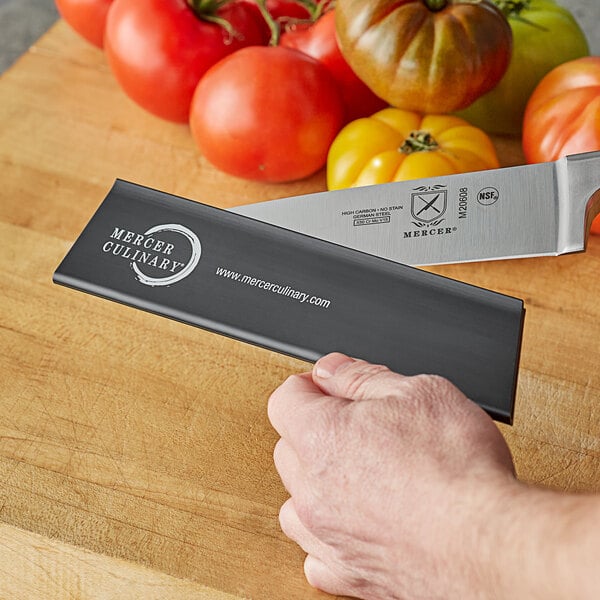 A hand using a Mercer Culinary knife blade guard to cover a knife.