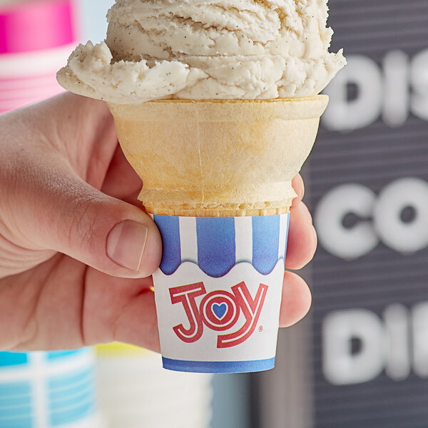 A hand holding a JOY flat bottom cake cone filled with ice cream.