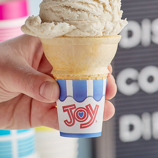 A hand holding a JOY cake cone filled with ice cream.