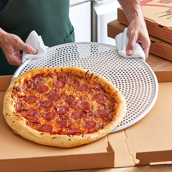 A hand using an American Metalcraft pizza screen to hold a pepperoni pizza.