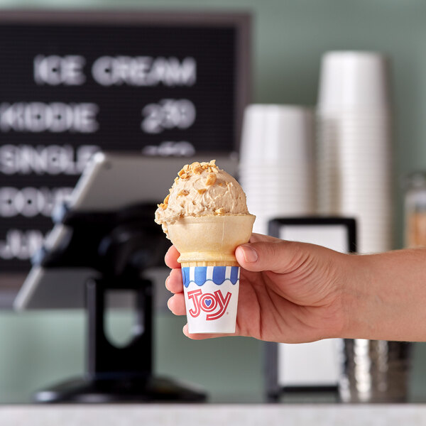 A hand holding a JOY flat bottom jacketed cake cone filled with ice cream.