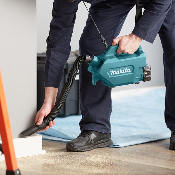 A person using a Makita handheld canister vacuum to clean a floor.