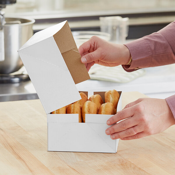 A person opening a white Baker's Mark box of donuts.