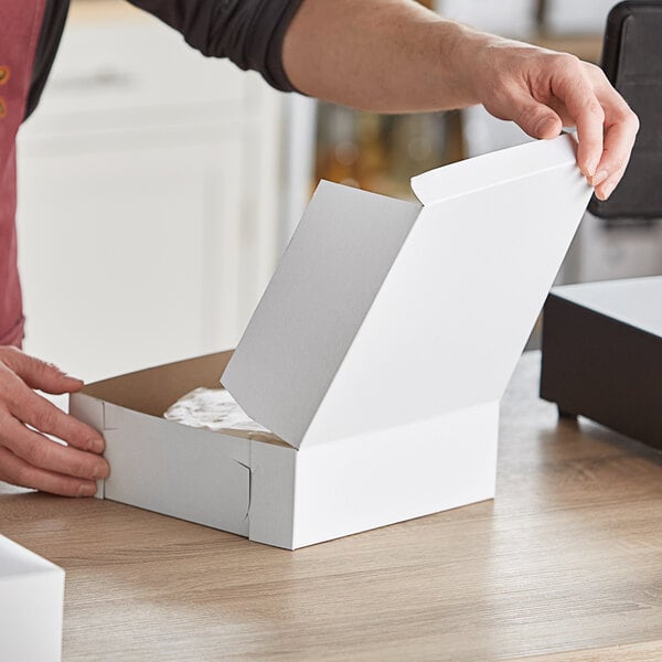 A hand opening a Baker's Mark white bakery box.