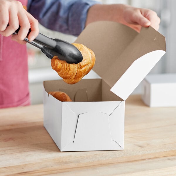 A person holding a croissant out of a white Baker's Mark bakery box.