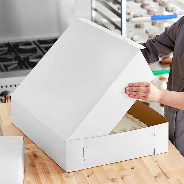 A person opening a white Baker's Mark bakery box.