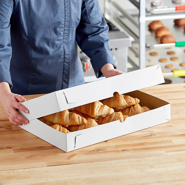 A person holding a white bakery box of croissants.