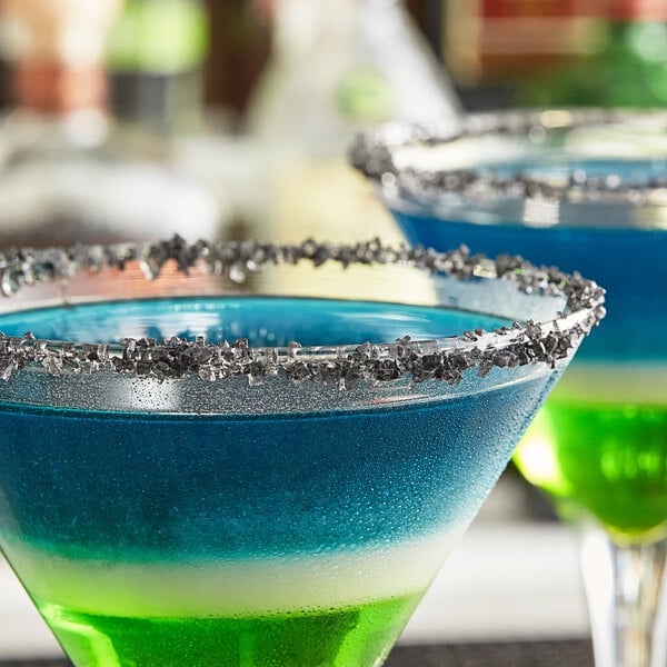 A close up of a blue drink with a black lava rim on a table in a cocktail bar.
