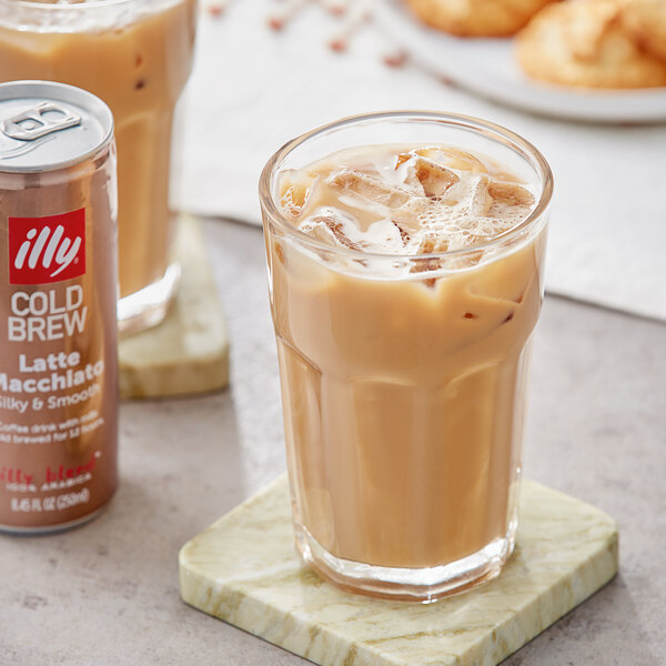 A glass of illy Cold Brew Latte Macchiato on ice with a brown illy can next to it.