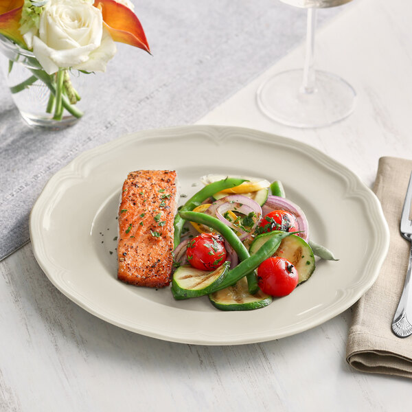 An Acopa Condesa porcelain plate with salmon and vegetables on a table.